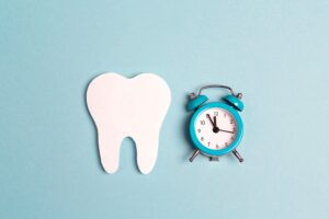 Model tooth next to blue alarm clock on a pale blue background